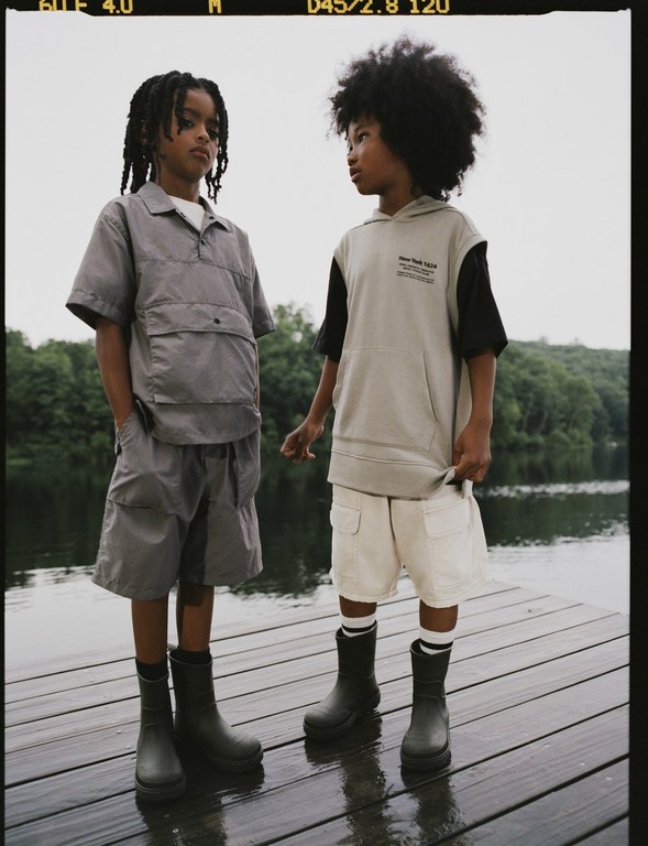 Two young boys standing on a wooden dock near a lake wearing casual outerwear and boots, portraying a relaxed outdoor style for kids.