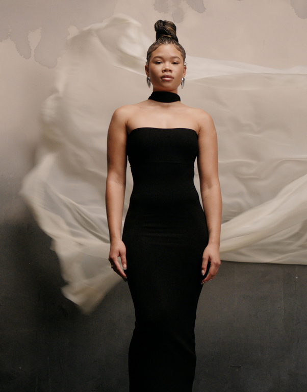 Portrait of a black woman in a strapless black dress against a soft abstract backdrop, showcasing elegant fashion and studio photography.