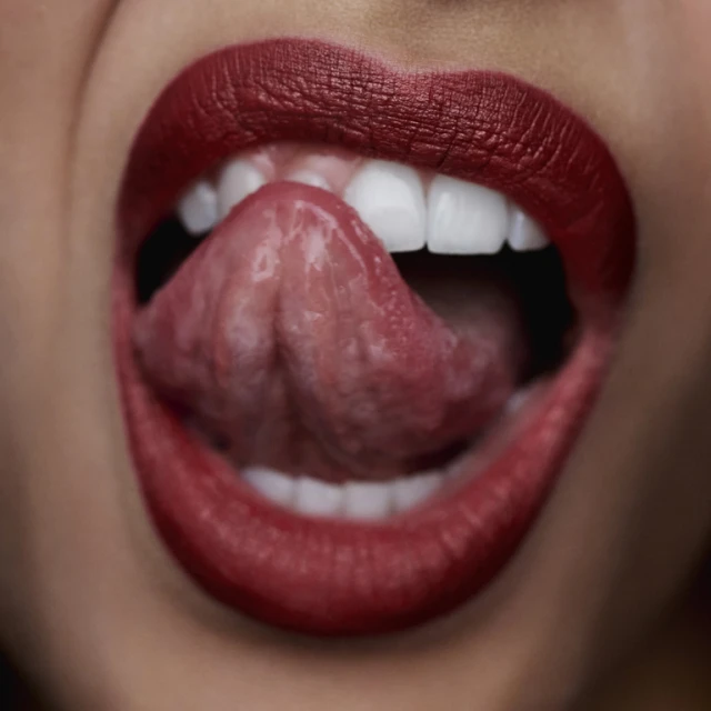 Close-up of a woman's face focusing on her open mouth, white teeth, and tongue sticking out, accented by bold red lipstick.