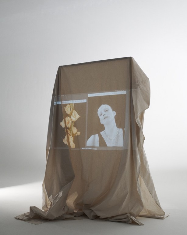 Abstract image of a beige fabric-draped structure displaying floral and portrait images on screens, set against a gradient white background.