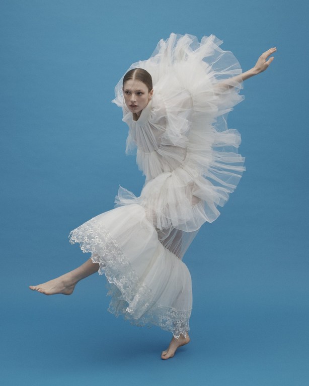 Fashion photography featuring a woman in an expressive pose wearing a white tulle gown on a blue background, showcasing movement and elegance.