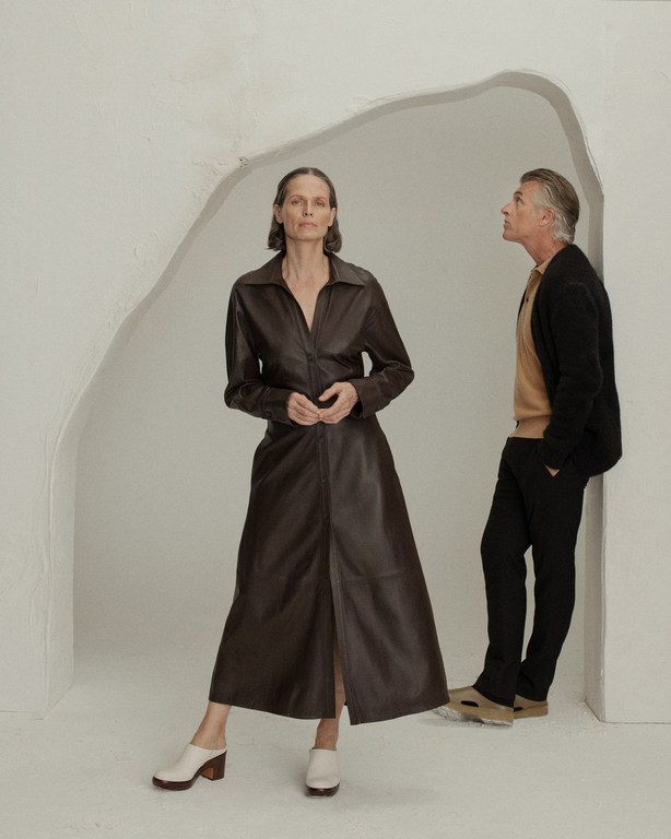 Woman in dark leather midi dress and man standing within a minimalist sculptural arch set designed by Caz Slattery.