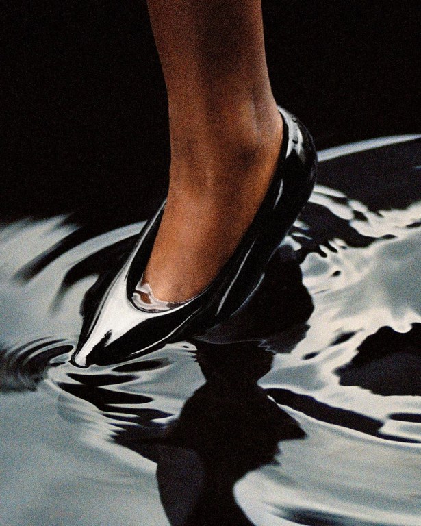 Close-up of a glossy black stiletto heel sinking into reflective rippled water, capturing dark elegance and fluid motion.