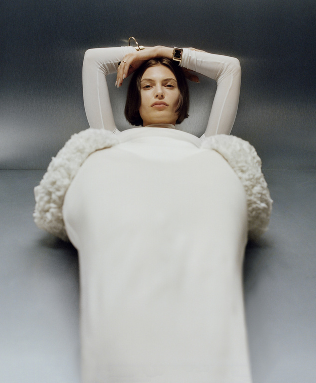 Low angle fashion portrait of a woman with short dark hair in a white long sleeve top against a grey metallic background by Mila Taylor-Young