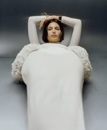 Low angle fashion portrait of a woman with short dark hair in a white long sleeve top against a grey metallic background by Mila Taylor-Young