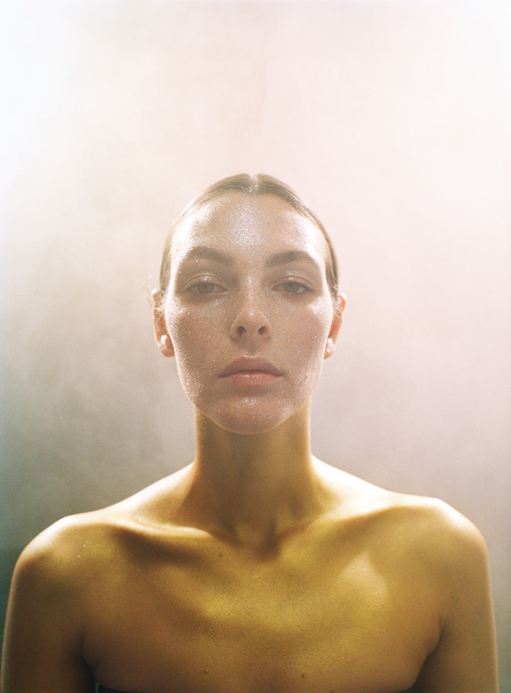 Close-up portrait of a woman with fair skin, bare shoulders, and wet face, set against a soft, blurred background. Beauty and fashion.