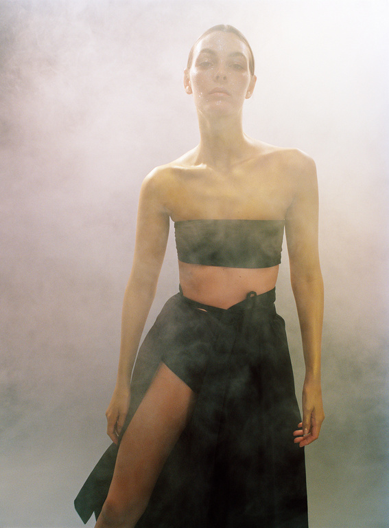 A woman in a strapless top and wrap skirt poses in a hazy studio setting with neutral colors. Fashion editorial shot.