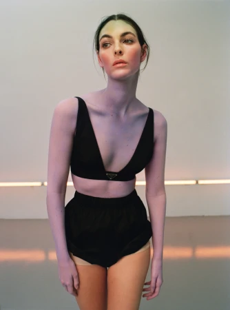 Model wearing a black crop top and black shorts posing in front of a plain background with a horizontal light fixture.