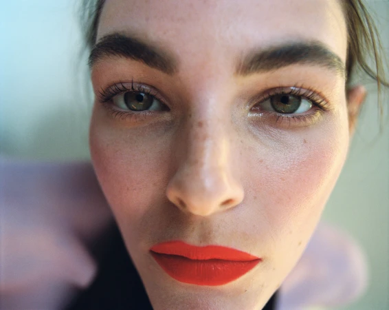 Close-up portrait of a woman with vibrant orange lipstick and defined eyebrows