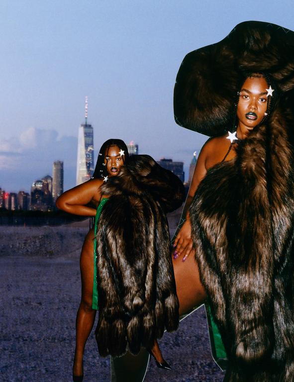 Two dark-skinned models in fur outerwear and star accessories strike poses against a blurred cityscape backdrop in an outdoor setting.