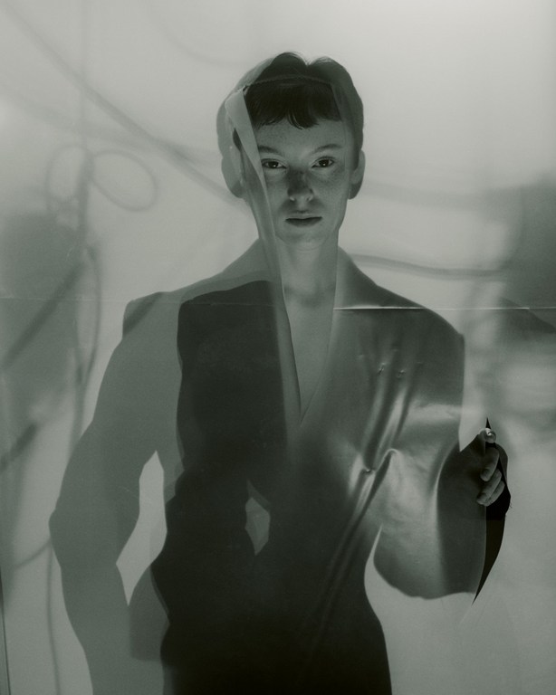 Portrait of a person peering through a torn translucent sheet with shadow projections behind them.