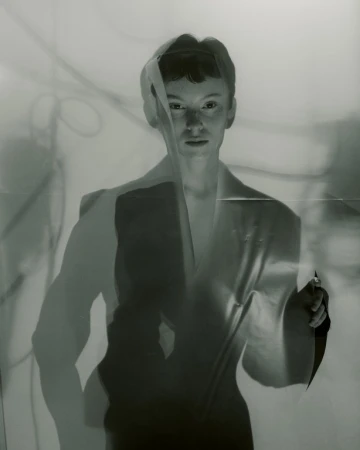 Portrait of a person peering through a torn translucent sheet with shadow projections behind them.