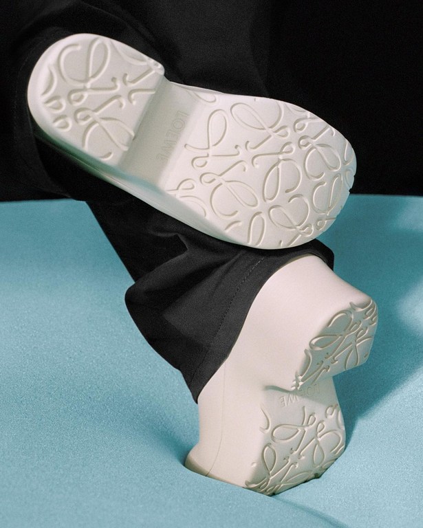 Two stacked orthopedic shoes showcasing patterned soles and black leggings against a blue surface and dark background.