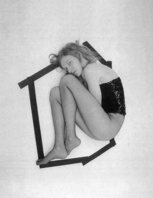 Young woman with fair skin and blonde hair posing inside a 2D black house frame on a white backdrop in a studio setting.