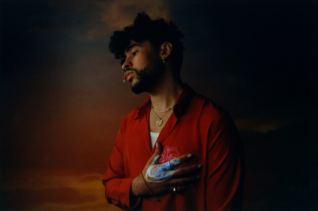 Profile shot of Bad Bunny in a red button-down shirt with an illustrated anatomical heart projected on his chest and hand.