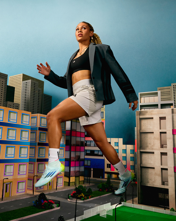 An athletic woman in sports attire and a blazer leaps confidently against a backdrop of stylized buildings, creating a surreal cityscape.