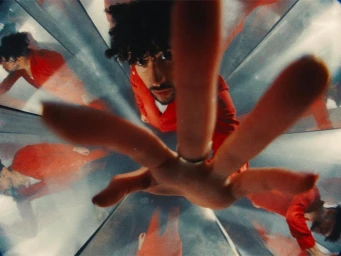 Man in red outfit reaching out toward the camera inside a kaleidoscopic mirrored tunnel designed by Rosie Turnbull.