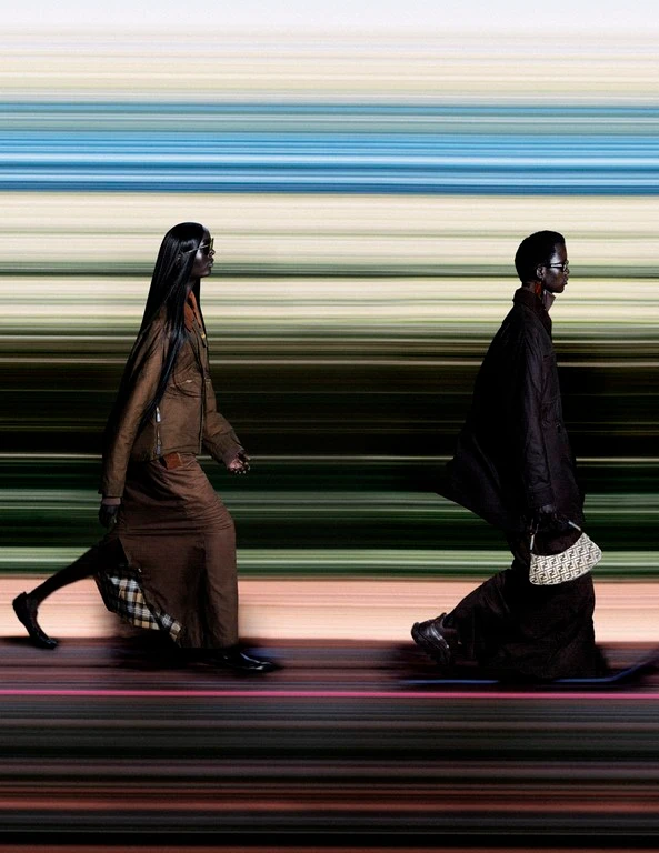 Two models walking on a runway against a motion-blurred horizontal striped background with choreography by Jordan Robson.