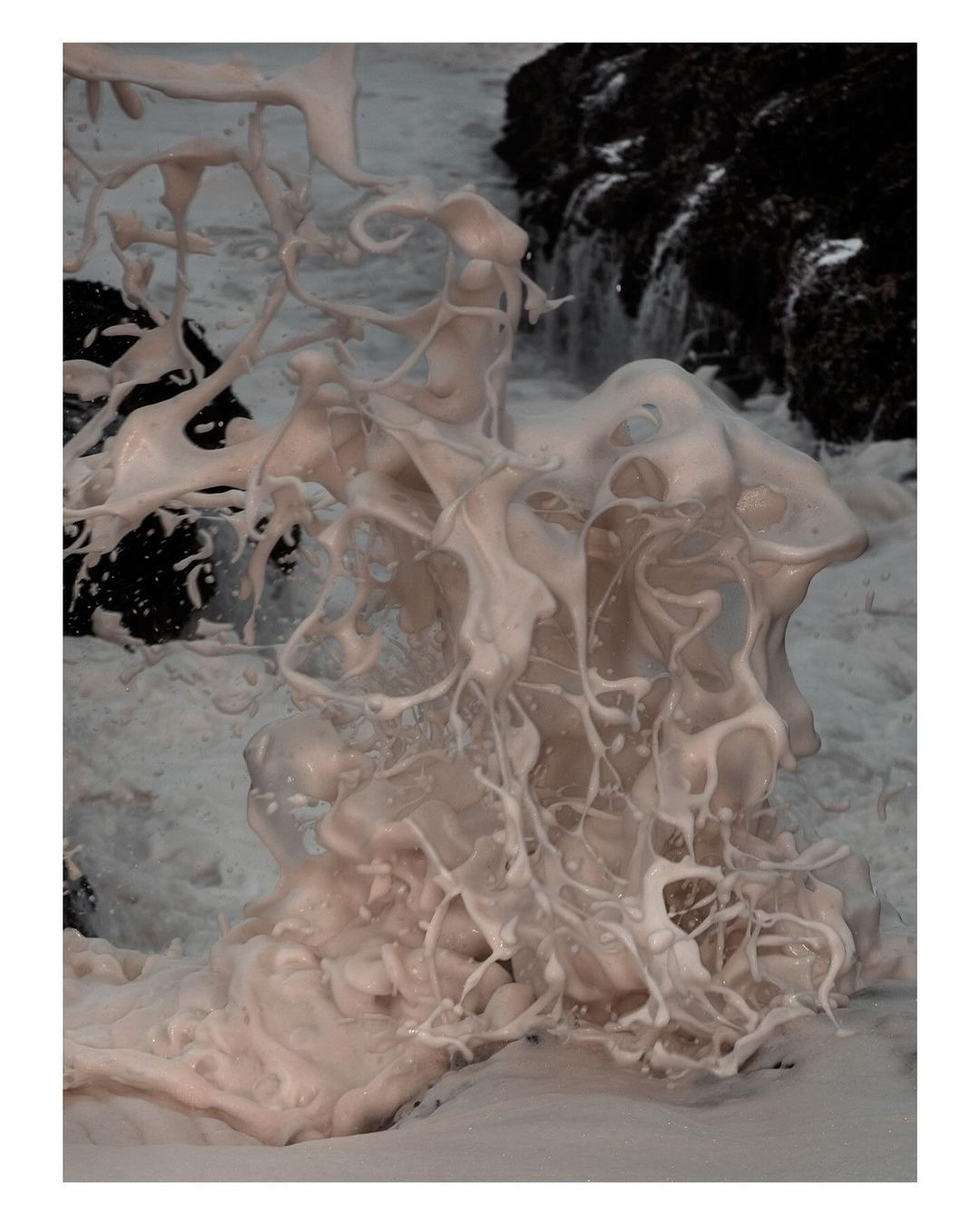 Close-up of white sea foam formation contrasting with dark rocks and ocean water, creating a dynamic coastal scene.