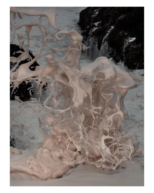 Close-up of white sea foam formation contrasting with dark rocks and ocean water, creating a dynamic coastal scene.