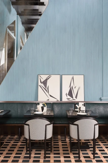 Modern restaurant interior featuring two chairs at tables with artwork on a striped, light-blue wall and checkered flooring.