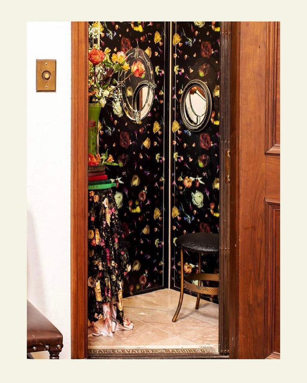 Eclectic entryway with floral wallpaper, an ornate mirror, and a vintage stool, bathed in soft lighting for a cozy, inviting atmosphere.