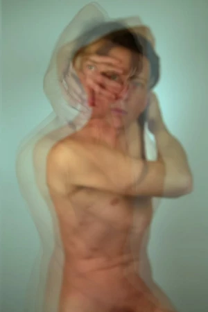 Abstract long exposure photograph of a nude adult with obscured face, against a pale blue background, creating a blurred, multi-layered effect.