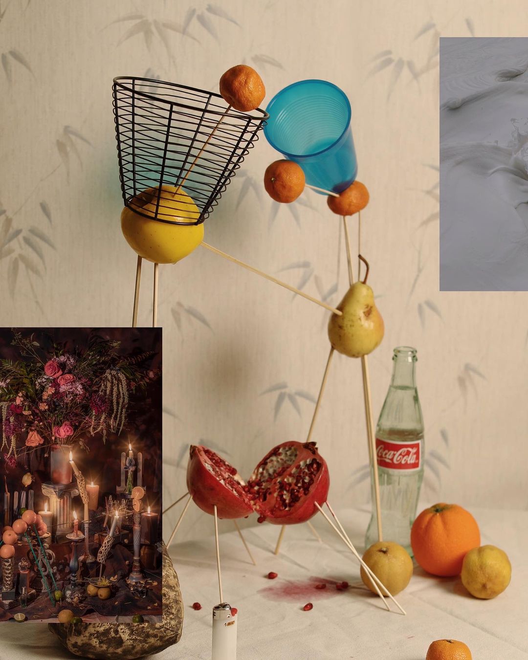 Still life composition featuring citrus fruits, a pear, and a pomegranate, supported by thin sticks, placed on a white surface.