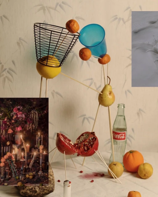 Still life composition featuring citrus fruits, a pear, and a pomegranate, supported by thin sticks, placed on a white surface.