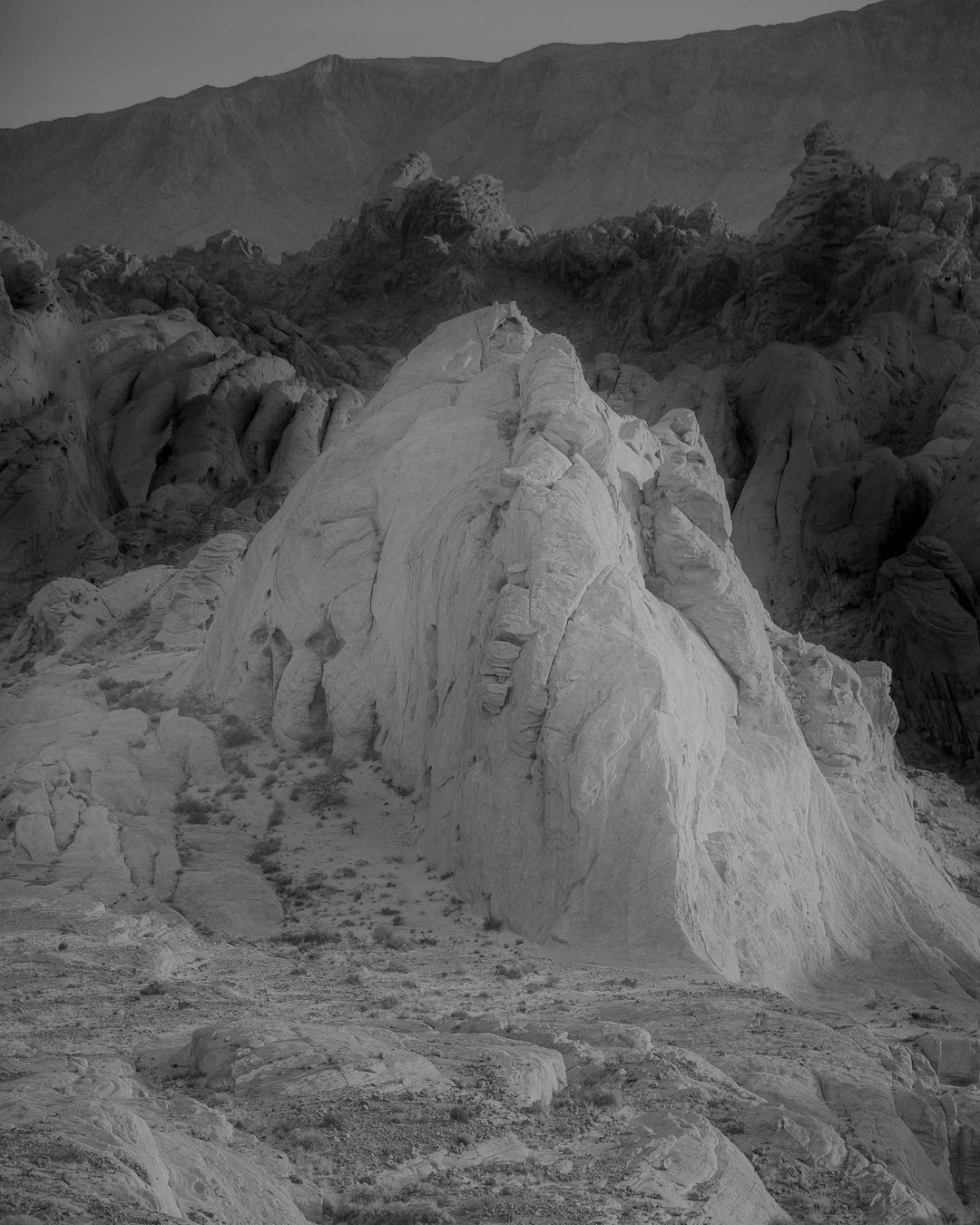 Monochromatic landscape featuring a large, light-colored rock formation in the foreground with a darker mountain range in the background.