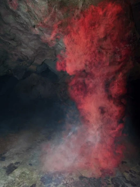 Abstract photography of a cave interior featuring a dark ceiling, ground, and a red smoke-like form dominating the image.