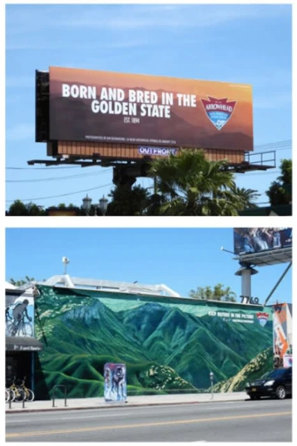 Billboard and mural art in an urban setting featuring mountains and commercial advertising, under a blue sky on a sunny day.