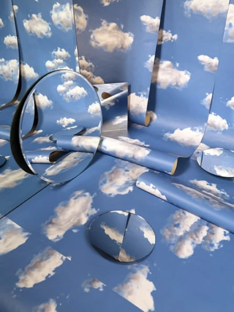 Artful composition of mirrors and cloud-patterned paper. Circular mirrors reflect sky and clouds. Blue and white color scheme.