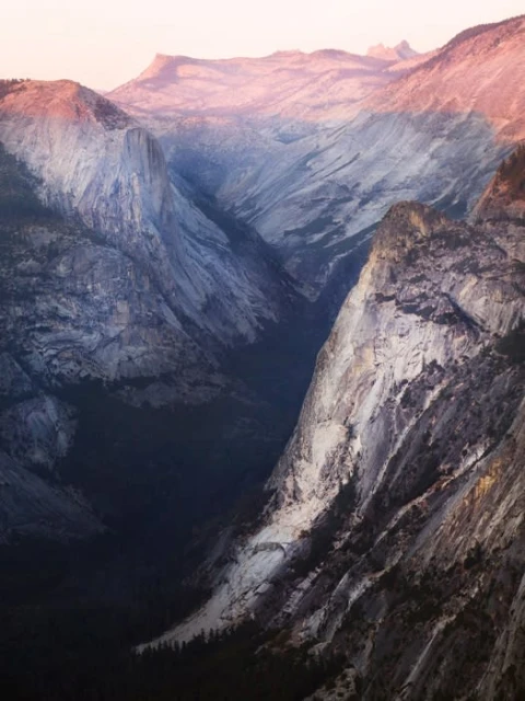 Yosemite Valley landscape view with gray granite rock formations, trees, and pinkish sky during the day in Yosemite National Park, USA.