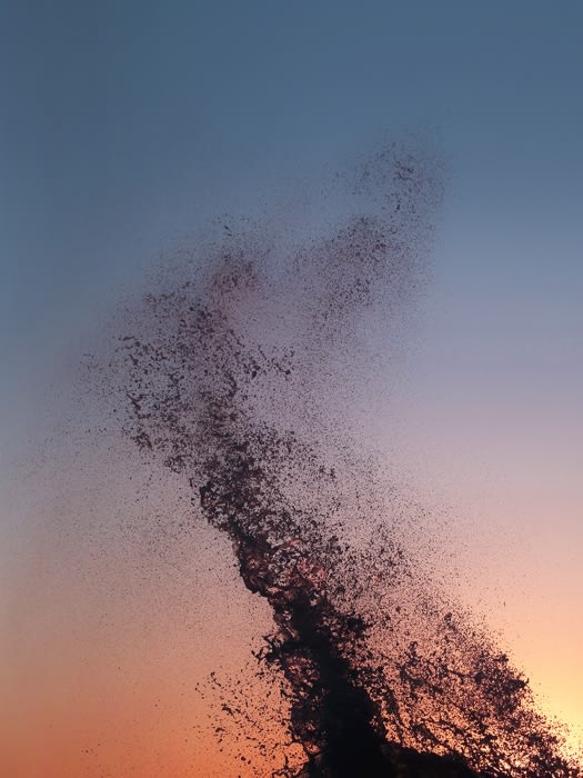 Dramatic photo of crashing ocean wave against a colorful sunset sky. Splashing water and dynamic shapes create a captivating natural scene.