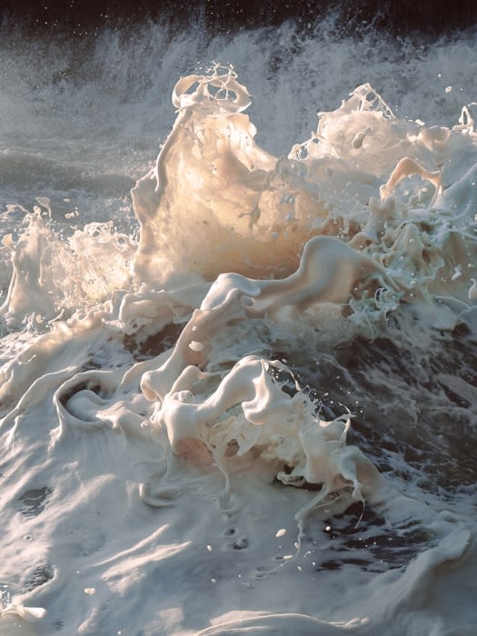 Dramatic ocean wave crashing with white foam and sea spray, illuminated by sunlight, creating a powerful and dynamic scene.