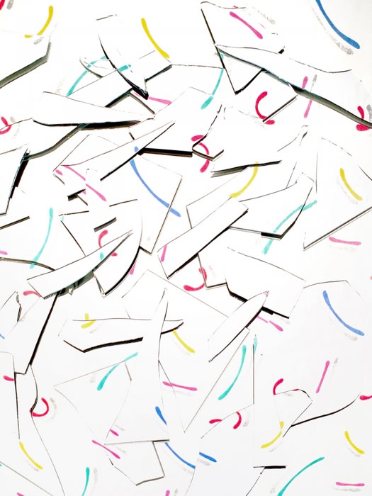 Abstract arrangement of white paper pieces with blue, yellow, pink, and teal curved line markings scattered on a white background.