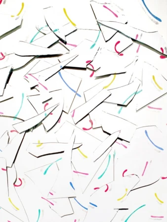 Abstract arrangement of white paper pieces with blue, yellow, pink, and teal curved line markings scattered on a white background.