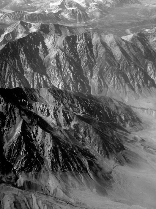 Monochrome aerial view of mountain range with snow-capped peaks and rugged terrain, showcasing dramatic landscape and natural beauty.