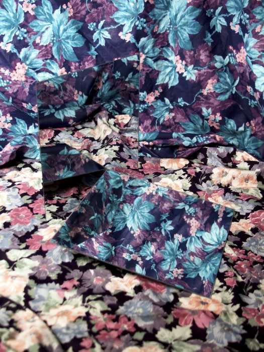 Floral-patterned fabric with mirrored surface reflecting the pattern, creating a refracted, repetitive visual effect with dark purples and blues.