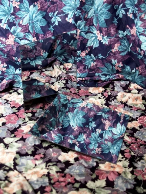 Floral-patterned fabric with mirrored surface reflecting the pattern, creating a refracted, repetitive visual effect with dark purples and blues.