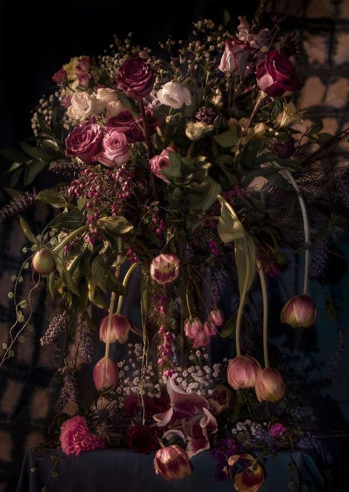 Dramatic floral arrangement featuring roses and tulips in a vintage style against a dark, textured background, creating a rich, moody aesthetic.