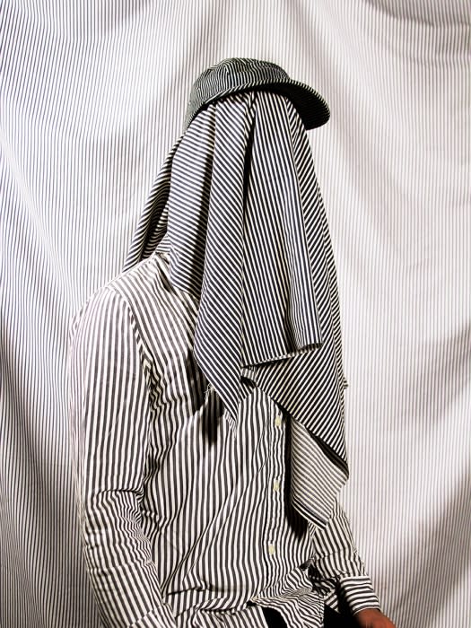 Person draped in a striped fabric and wearing a striped cap stands against a striped background, creating a cohesive monochrome look.