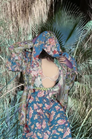 Model in blue floral hooded shirt and matching skirt standing amidst dense tropical foliage by Delaney Allen