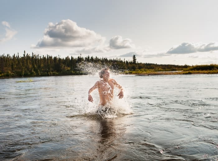 A person splashes in a river surrounded by a forest and cloudy sky, creating a dynamic scene that captures the freedom of outdoor activities.