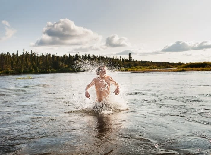 A person splashes in a river surrounded by a forest and cloudy sky, creating a dynamic scene that captures the freedom of outdoor activities.