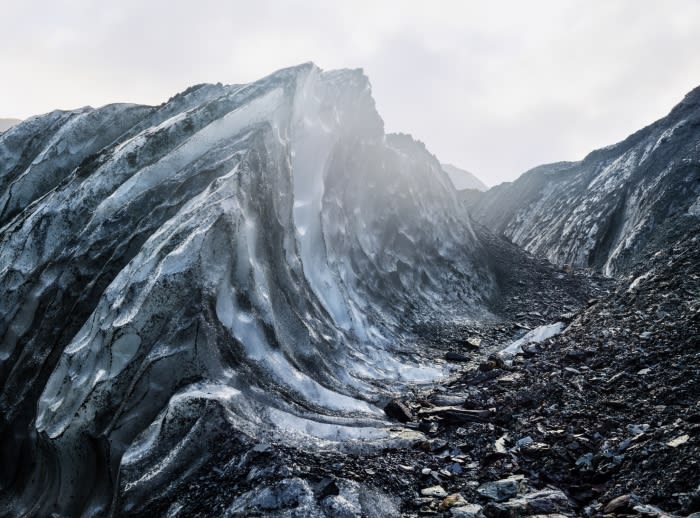 Detailed view of a glacier with blue ice formations and dark rock terrain on a cloudy day, showcasing nature's textures and patterns.
