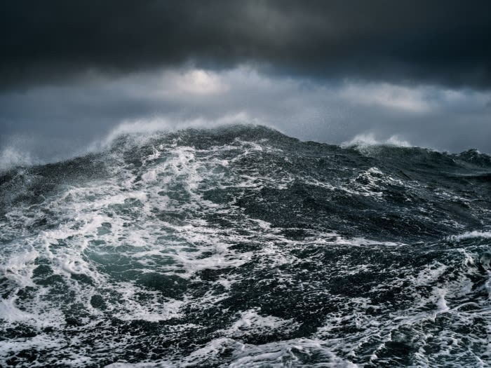 A dramatic ocean scene with turbulent dark water, white foam, and a dark, overcast sky filled with storm clouds creating a powerful visual.