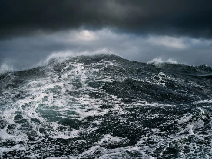 A dramatic ocean scene with turbulent dark water, white foam, and a dark, overcast sky filled with storm clouds creating a powerful visual.