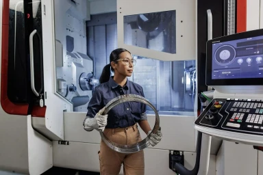 Woman in navy shirt holding metal ring inside industrial factory near CNC machine